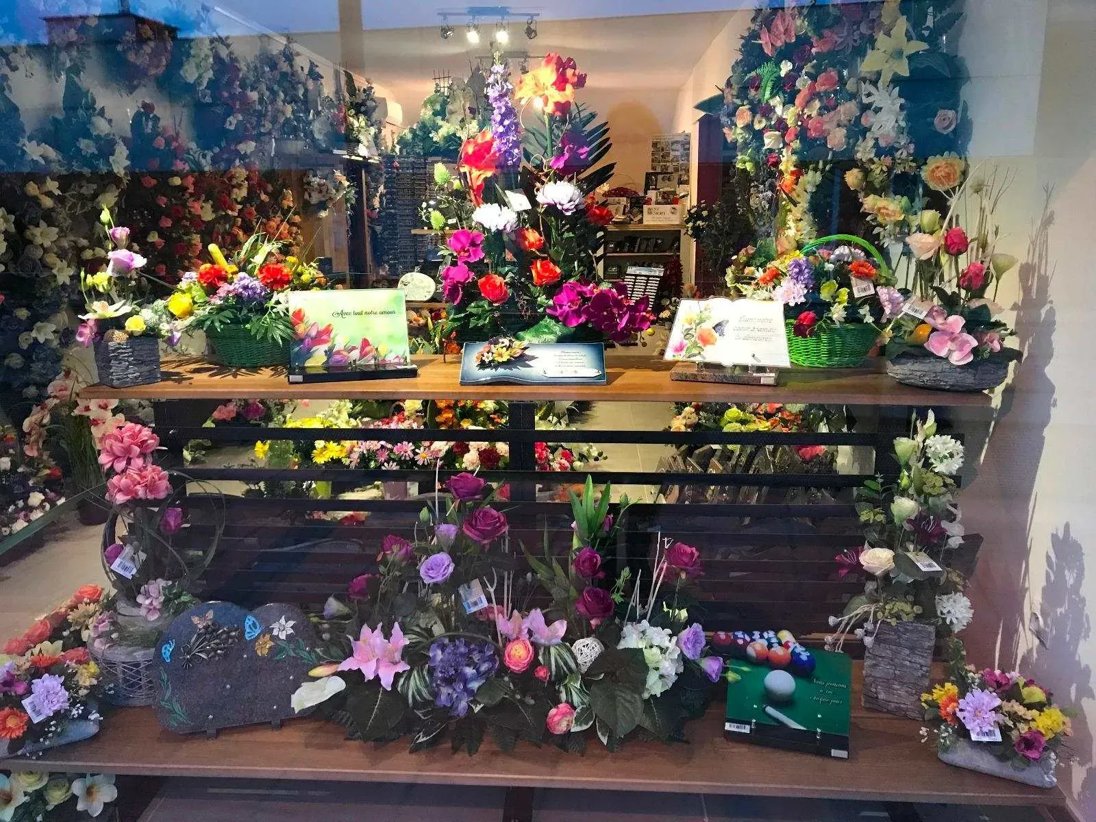 Vitrine de pompes funèbres exposant des compositions florales colorées et plaques.