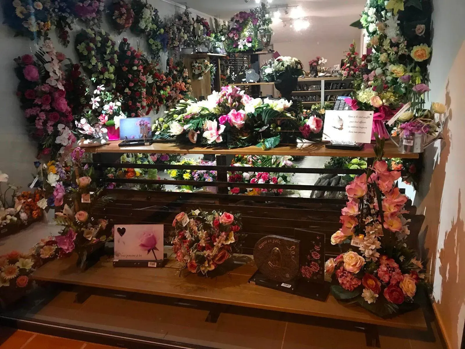 Exposition d'articles funéraires, fleurs artificielles et souvenirs en vitrine.